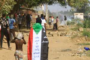 Un hombre envuelto en una bandera de Sudán observa cómo las fuerzas de seguridad sudanesas disparan gases lacrimógenos contra los manifestantes durante una manifestación que pide un gobierno civil y denuncia la administración militar, en la ciudad gemela de Umdurman, la capital de Jartum, el 30 de noviembre de 2022.