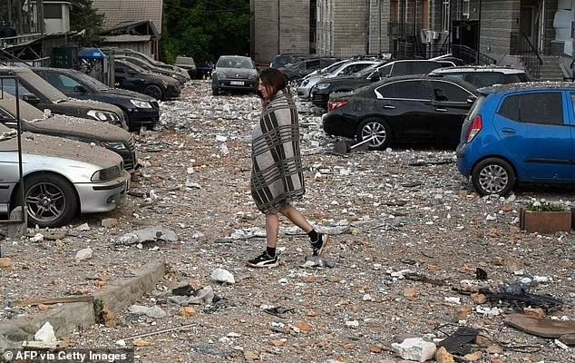 Un residente local camina entre autos dañados al salir de un edificio residencial de varios pisos, parcialmente destruido después de los ataques nocturnos con drones en Kiev el 30 de mayo de 2023.