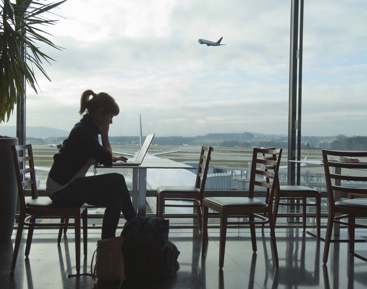 Mujer consultando su computador mientras aguarda en un aeropuerto - Imagen de referencia