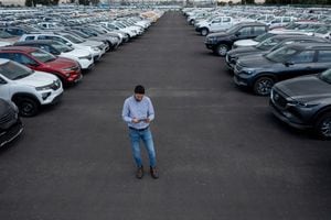 Latin American salesman using a tablet while being surrounded by cars at the dealership