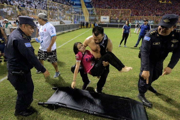 Los partidarios son ayudados por otros tras una estampida durante un partido de fútbol entre Alianza y FAS en el estadio Cuscatlán en San Salvador,